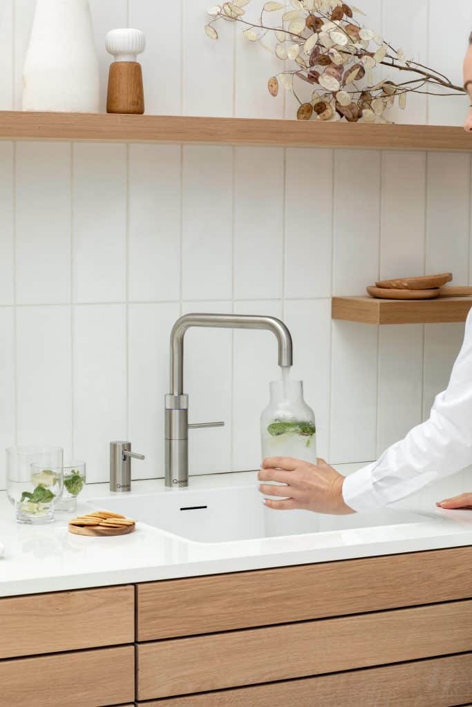 Frau befüllt Glasflasche mit Sprudelwasser aus einem Quooker Wasserhahn