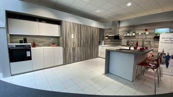 Weiße Küche mit silbernen Griffe kombiniert mit grauen Holzelementen, integrierter Frühstückstheke, erhöhtem Backofen und roten Akzenten