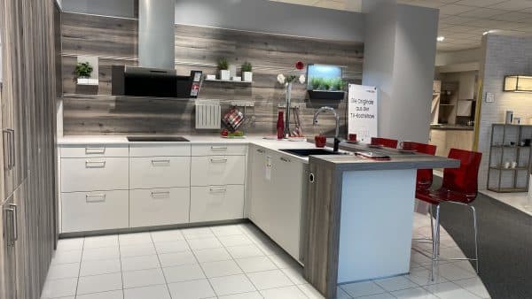 Weiße Küche mit silbernen Griffe kombiniert mit grauen Holzelementen, integrierter Frühstückstheke, erhöhtem Backofen und roten Akzenten