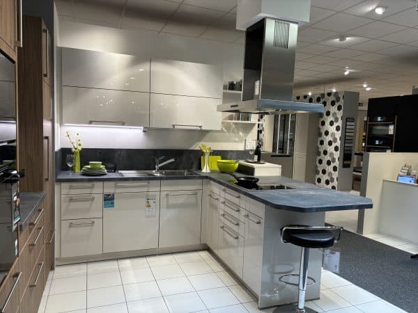kleine weiße L-Küche in Hochglanz mit langen silbernen Griffen, dunkler Arbeitsplatte und integrierter Frühstückstheke