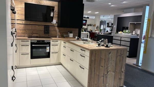 helle einladende U-Küche mit schwarzen Griffen, erhöhtem Backofen, viel Stauraum, Arbeitsfläche in Holzoptik und weißem Spülbecken