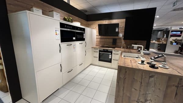 helle einladende U-Küche mit schwarzen Griffen, erhöhtem Backofen, viel Stauraum, Arbeitsfläche in Holzoptik und weißem Spülbecken